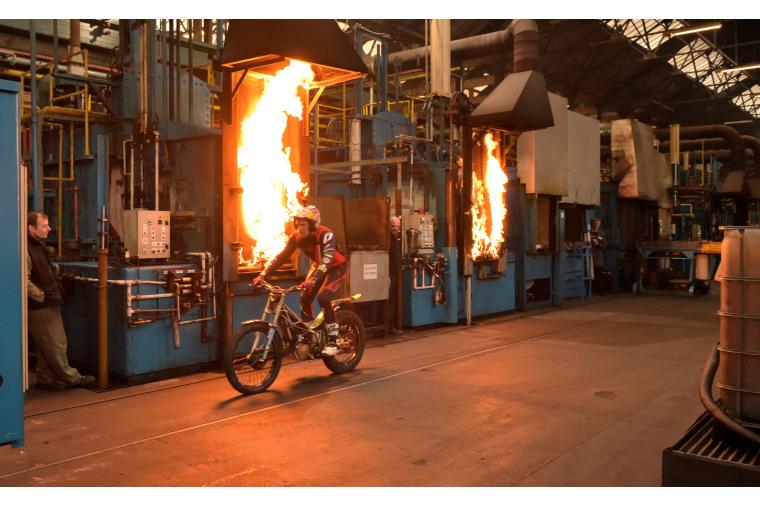1a) 12 times Trials World Champion, Dougie Lampkin, rides past flaming furnaces at Wallwork Heat Treatment